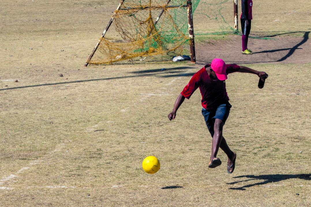 A man shows off his shooting skills to his friends at the Dlepu soccer stadium, Joza. © Siphamandla Boma.